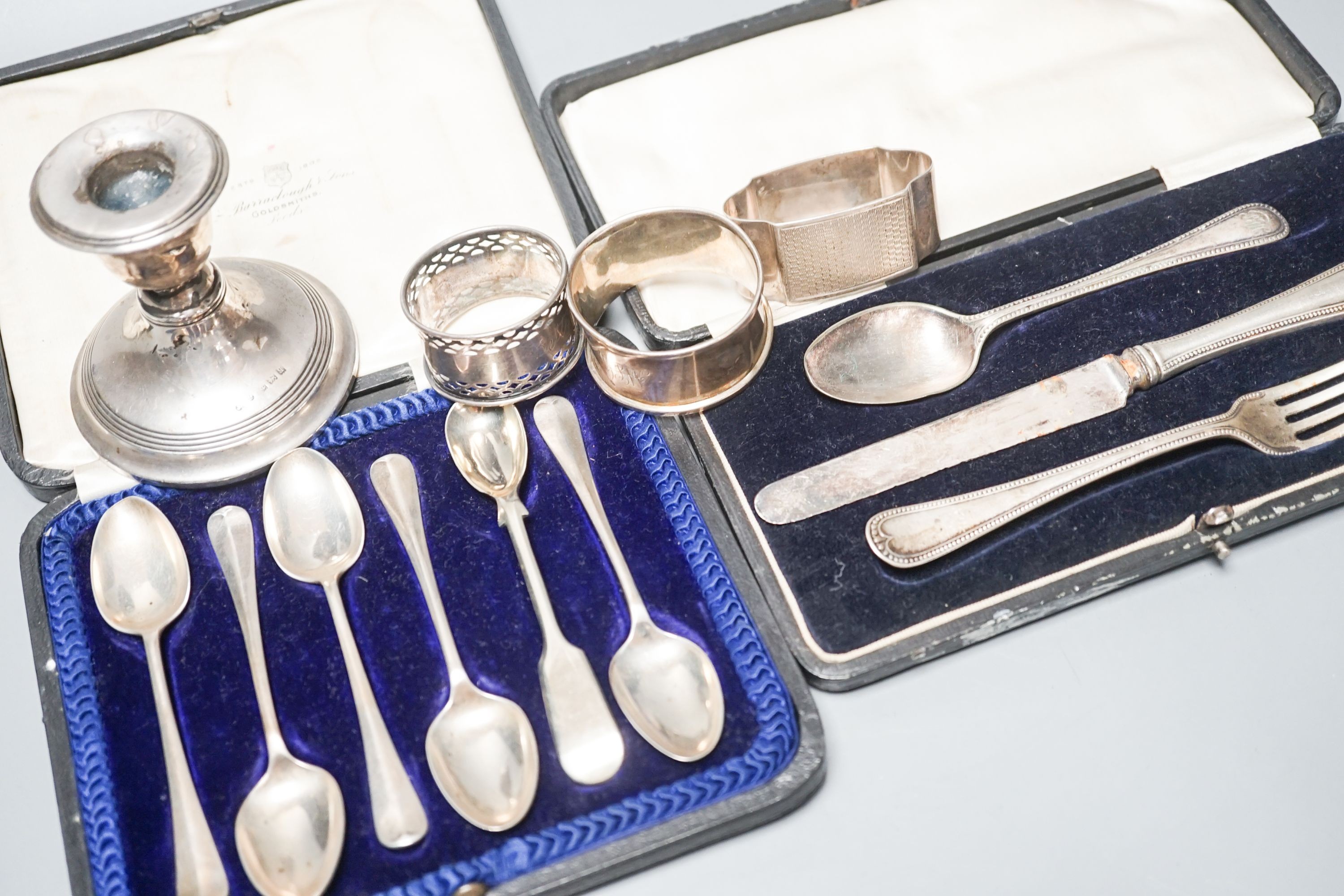 A cased set of six silver teaspoons, a cased christening set, three silver napkin rings and a silver dwarf candlestick.